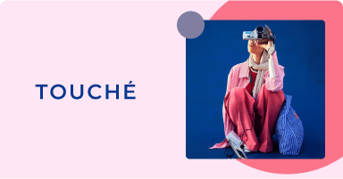 Model wearing pink and red clothing, holding a camera, representing the Touché brand.